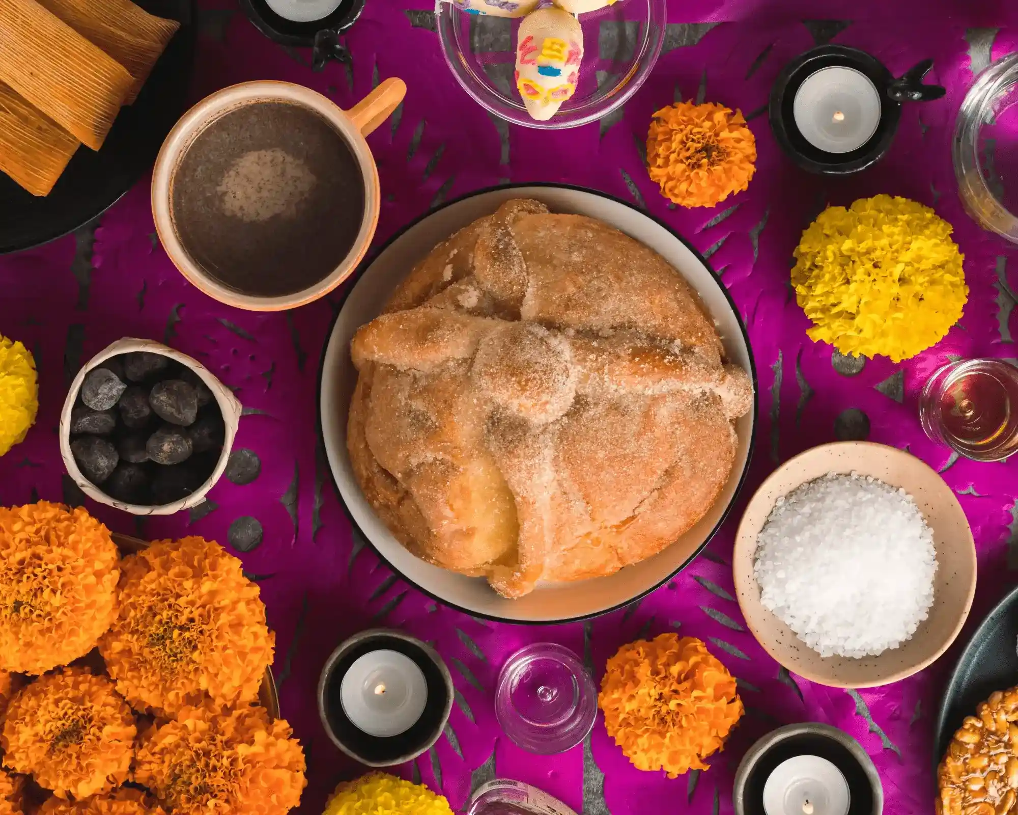 image of pan de muerto on a table orned with candles and flowers